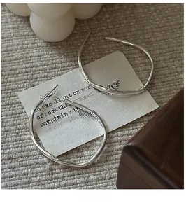 Close-up of minimalist S925 sterling silver irregular hoop earrings on fabric