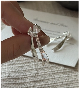 Detail of silver bow earrings with textured surface held to show scale and craftsmanship