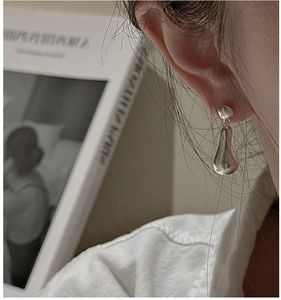 Macro detail of silver teardrop earrings with a polished finish worn by a model