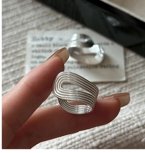 Macro detail of silver rings with a multi-layered wavy textured design on fabric