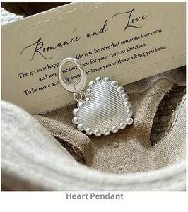 Detail of S925 silver heart pendant with ribbed texture and lobster clasp on linen cloth