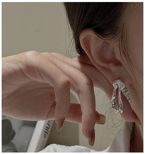 Close-up of stylish liquid metal silver bow earring worn by model in soft lighting