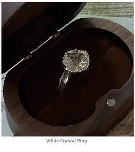 Macro detail of firework-cut clear crystal ring in textured silver setting on dark wood box