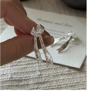Detailed view of silver bow earrings with textured ribbon design on a fabric background