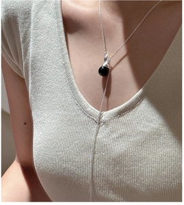 Close-up of a delicate silver necklace with a polished black bead on a ribbed sweater