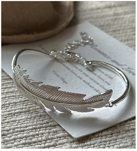Detailed view of silver feather bangle featuring intricate texture and adjustable chain