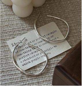 Detailed view of silver S925 irregular wavy hoop earrings on a textured fabric backdrop