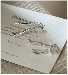 Detail of silver ribbon bow earrings displayed on white paper and beige knit fabric