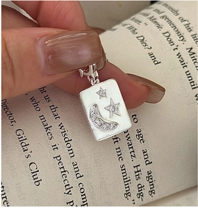 Detailed macro of a rectangular silver S925 star and moon pendant with white enamel