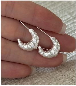 Detailed view of sterling silver croissant earrings with matte wrinkled texture finish