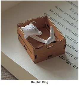 Macro shot of white matte dolphin ring with subtle texture on miniature wooden crate