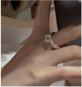 Macro detail of silver ring with white crystal and braided texture on finger