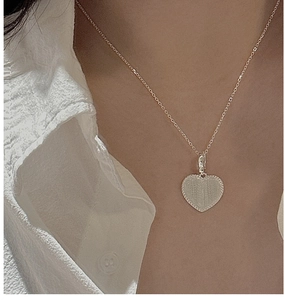 Détail d'un pendentif coeur en argent S925 avec bords perlés sur une chemise blanche