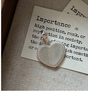Vue détaillée du pendentif cœur en argent S925 avec texture mate sur tissu beige