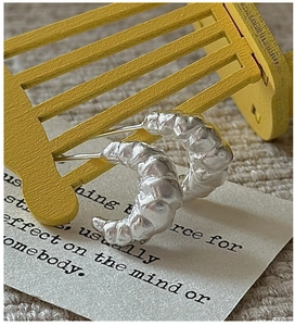 Macro detail of silver croissant earrings with textured surface on minimalist backdrop