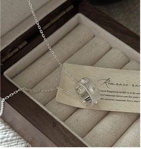 Gros plan du pendentif cylindre en argent S925 avec texture florale dans l'écrin