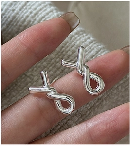 Close-up of hand holding silver knot stud earrings against a beige knit background
