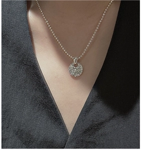 Macro detail of a 925 silver ball chain necklace with a full-diamond round disc pendant