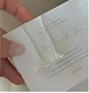 Detail of silver lily flower earrings with matte brushed texture on elegant long hooks