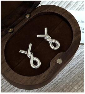 Macro shot of silver minimalist cross-knot earrings on a luxury wooden jewelry box