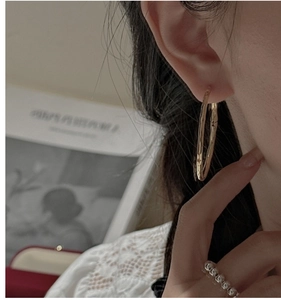 Gros plan d'une boucle d'oreille créole dorée avec texture martelée sur un mannequin