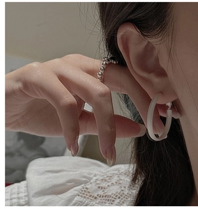 Close-up of matte white hoop earrings and a beaded silver ring worn in a cozy setting