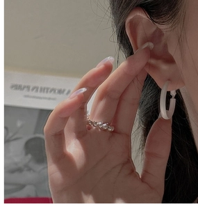 Close-up of a matte white C-shaped earring and a minimalist beaded silver ring on model