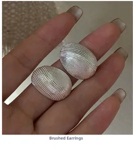 Macro shot of silver earrings featuring brushed texture and woven mesh details