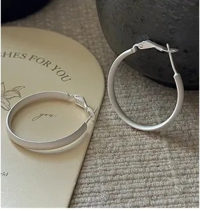 Close-up of matte silver hoop earrings on beige fabric with minimalist artistic card