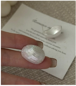 Detail of silver stud earrings with textured relief and matte finish held by hand