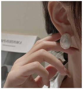 Close-up of matte silver oval earring with frosted texture worn on female model ear