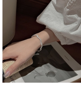 Detail of minimalist S925 sterling silver wavy braided bracelet on female wrist