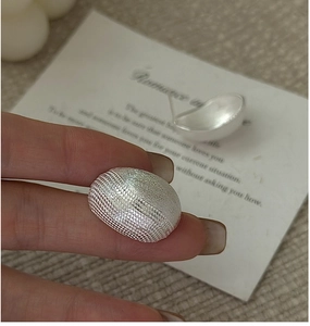 Close-up of S925 sterling silver stud earrings with textured matte finish on hand