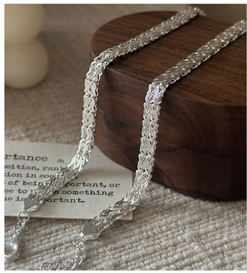 Detail of S999 silver woven chain with lobster clasp and heart charm on a wooden box