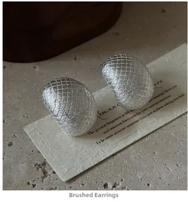 Macro shot of silver stud earrings featuring a cross-brushed matte metal texture