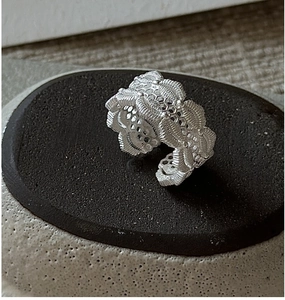 Macro shot of silver lace hollow patterned open ring on dark textured stone base