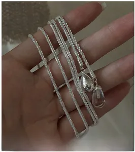 Detail of S925 silver necklace featuring double teardrop crystal pendants held in hand