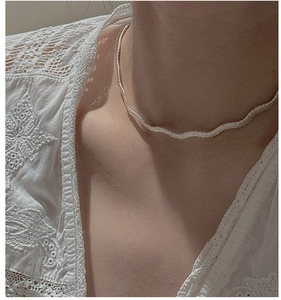 Gros plan d'un collier blanc tissé en forme de vague porté avec un haut en dentelle