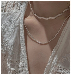 Détail du collier tressé en argent S925 superposé à un ras-du-cou blanc sur le cou