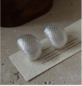 Macro shot of S925 silver stud earrings with brushed lattice texture on stone surface