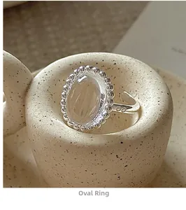 Macro detail of oval white crystal ring with silver beaded bezel on ceramic surface