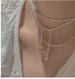 Detail of layered S925 silver chain necklace with teardrop pendants on lace clothing