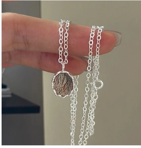 Detail of silver S925 necklace featuring an oval rutilated quartz pendant and box chain