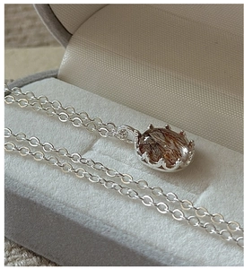 Macro shot of silver S925 necklace with oval rutilated quartz in crown prong setting