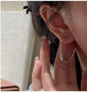 Close-up of a model wearing large C-shaped silver earrings with a hammered texture
