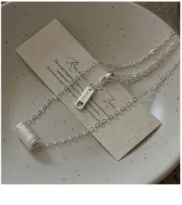 Dettaglio collana in argento S925 con pendente cilindrico opaco su carta vintage