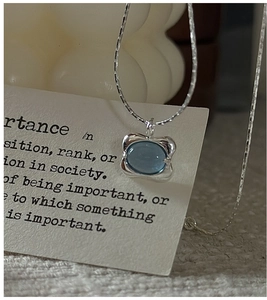 Macro detail of S925 silver necklace with oval light blue gemstone in wavy liquid metal frame