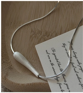 Macro view of matte teardrop silver pendant on a flat snake chain necklace
