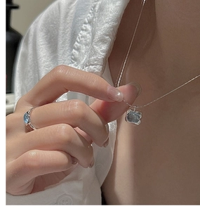 Detail of light blue gemstone necklace and open ring set on a model in a warm setting