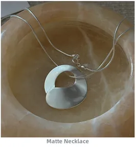 Close-up of matte S925 sterling silver irregular ring necklace in a marble texture bowl